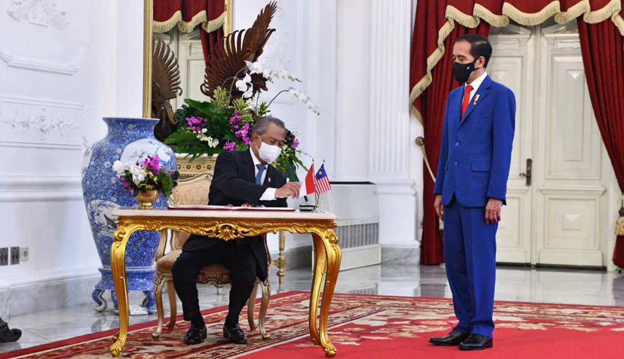 Presiden Indonesia Joko Widodo (kanan) menyaksikan Perdana Menteri Malaysia Muhyiddin Yassin menandatangani buku tamu di Istana Merdeka, Jakarta, Jumat (5/2/2021). Pertemuan di antaranya membahas isu perlindungan WNI, isu kawasan, dan isu global. (HANDOUT/INDONESIAN PRESIDENTIAL PALACE/AFP)