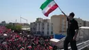 Seorang pria memegang bendera Iran saat truk yang membawa peti jenazah Pemimpin Tertinggi Iran Ayatollah Ali Khamenei dan anggota keluarganya yang terbunuh melintas  di Teheran, Iran, Senin, 6 Juli 2026. (AP Photo/Vahid Salemi)