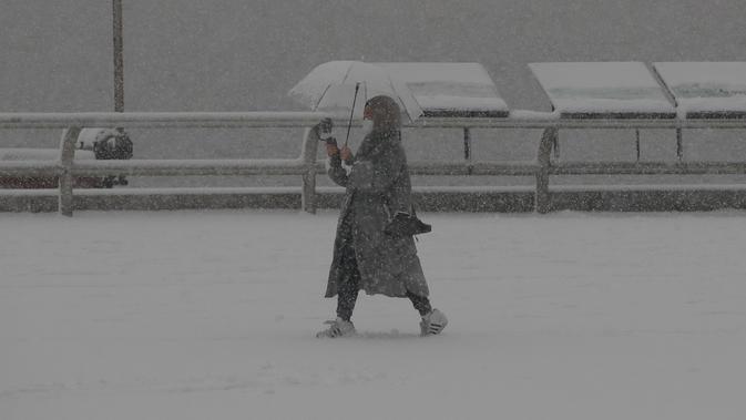 Seorang wanita memakai masker sebagai pencegahan virus corona berjalan di salju di Goyang, Korea Selatan, Kamis (28/1/2021). Lebih dari 15 sentimeter salju diperkirakan akan turun di daerah pegunungan di Pulau Jeju dan daerah pedalaman timur di Provinsi Jeolla hingga Jumat pagi. (AP/Lee Jin-man)