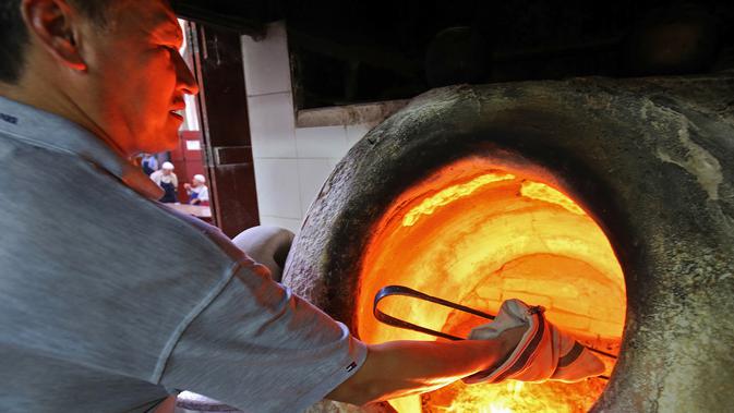 Tukang roti mengangkat roti Iran atau taftoon yang sedang dipanggang dalam oven tradisional di sebuah toko di Kuwait City, Kuwait, 27 Juni 2019. Selesai dipanggang, pembuat roti akan mengeluarkan roti menggunakan tongkat panjang. (YASSER AL-ZAYYAT/AFP)