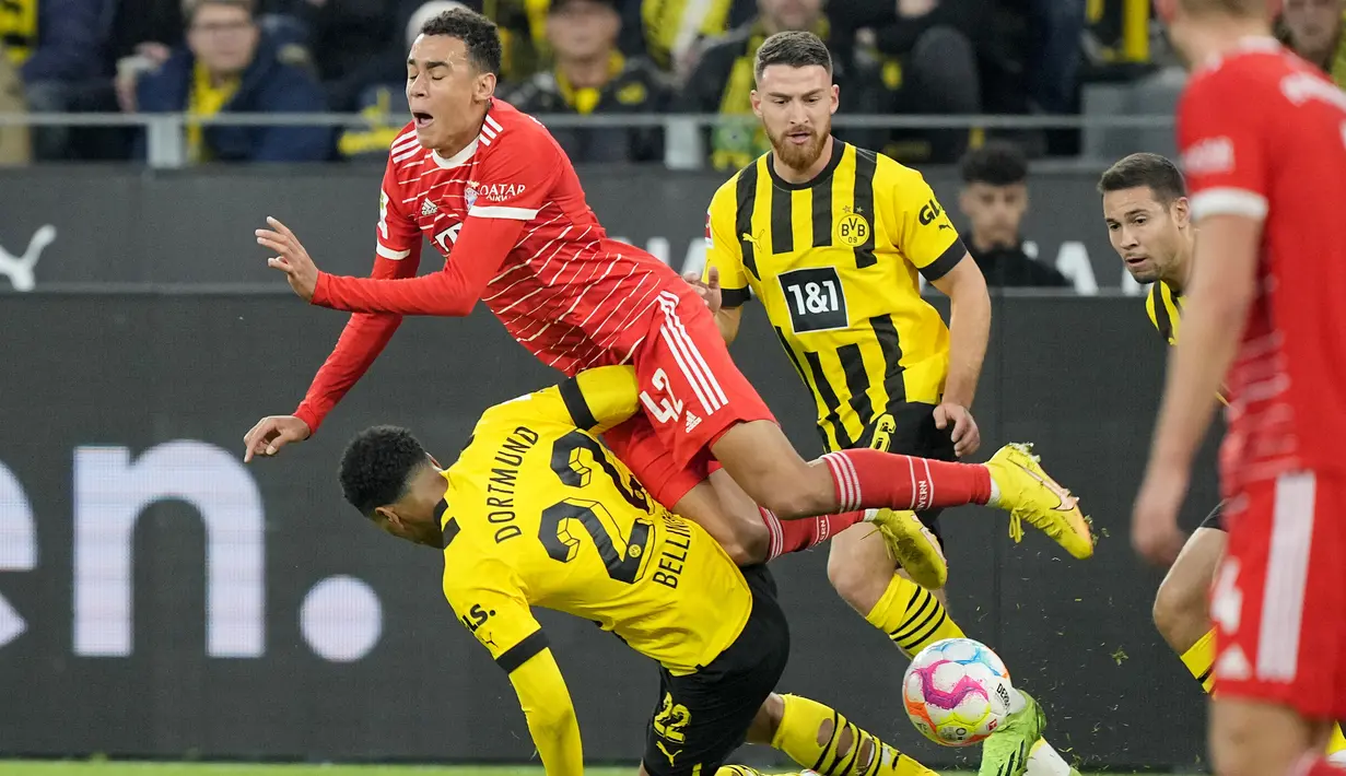 Penyerang Bayern Munchen Jamal Musala jatuh di atas gelandang Borussia Dortmund Jude Bellingham dalam laga lanjutan Bundesliga, kasta tertinggi Liga Jerman, musim 2022-2023, di Signal-Iduna Park, Sabtu (9/10/2022). Borussia Dortmund berhasil menahan imbang Bayern Munchen dengan skor imbang 2-2. (AP Photo/Martin Meissner)