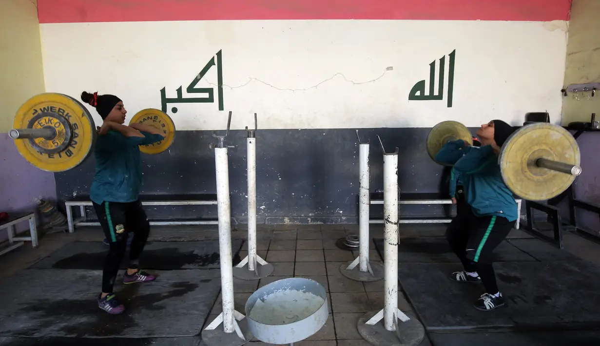 Dua atlet angkat besi wanita mengangkat beban saat berlatih di klub di Kota Sadr, sebelah timur Baghdad, Irak (18/1). Jika menang dan membawa medali, hal tersebut dapat membantu meringankan beban keuangan keluarga mereka. (AFP Photo/Ahmad Al-Rubaye)