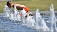 Seorang anak mendekatkan wajahnya pada air mancur saat menikmati musim panas di Nantes, Prancis barat, Senin (19/6). Suhu temperatur di Prancis mencapai 36 derajat celcius. (AFP Photo / LOIC VENANCE)