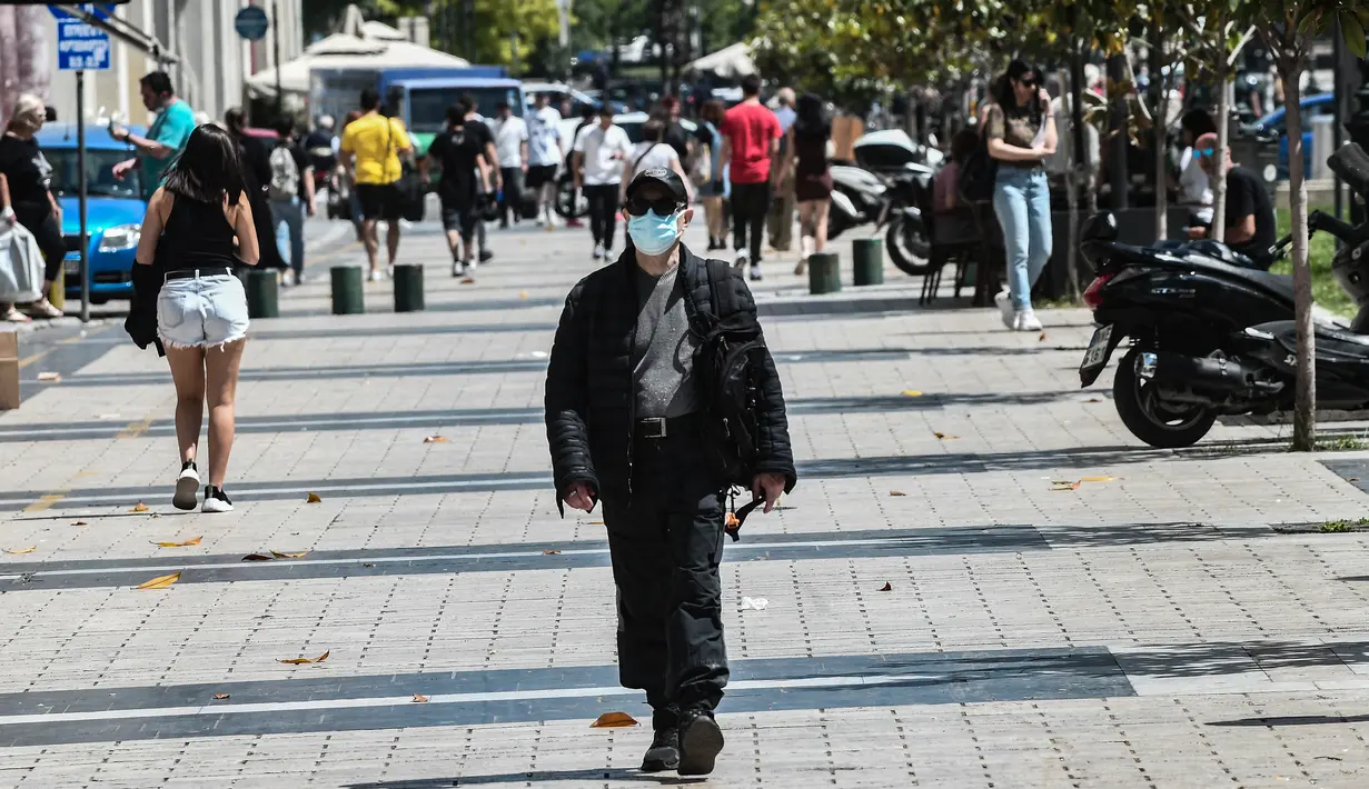 Seorang pejalan kaki berjalan di jalan mengenakan masker di pusat Thessaloniki, Yunani utara (18/5/2022). Mulai 16 Mei, masker wajah tidak lagi diperlukan di banyak penerbangan di Uni Eropa, tetapi Yunani telah mempertahankan aturan maskernya. (AFP/Sakis Mitrolidis)