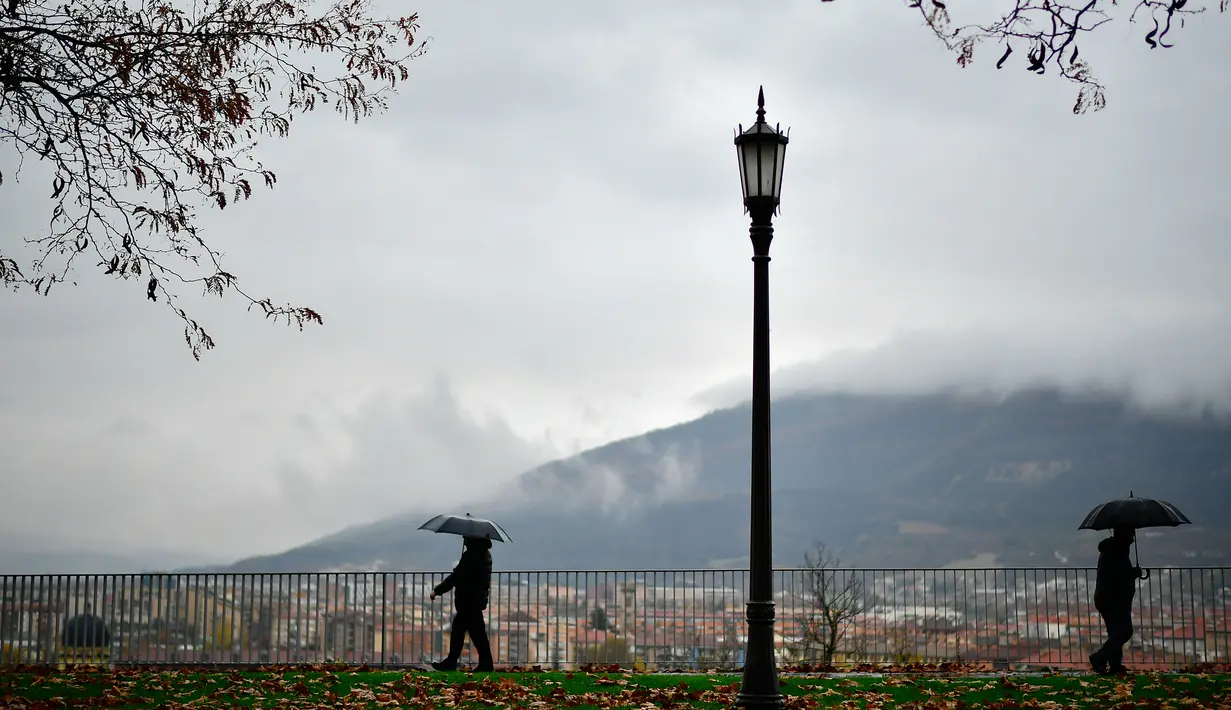 Pejalan kaki memakai payung menyusuri jalanan yang penuh dengan daun saat musim gugur di Pamplona, Spanyol, Selasa (20/11). (AP Photo/Alvaro Barrientos)