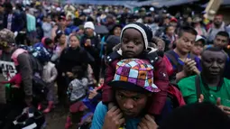 Seorang migran Haiti yang membawa seorang anak laki-laki bersiap untuk memulai penyeberangan Celah Darien  dari Kolombia ke Panama Sabtu, (15/10/2022). Perjalanan Kelompok Imigran tersebut berharap mencapai Amerika Srikat (AS).(Fernando Vergara/AP)