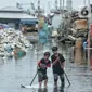 Anak-anak bermain air saat banjir Rob melanda kawasan Pelabuhan Perikanan Samudera Nizam Zachman, Muara Baru, Jakarta Utara, Selasa (27/12/2022). Penjabat (Pj) Gubernur DKI Jakarta Heru Budi Hartono meminta masyarakat pesisir agar waspada menghadapi banjir Rob yang berdasarkan prediksi Badan Penanggulangan Bencana Daerah (BPBD) DKI Jakarta akan terjadi di kawasan pesisir Jakarta hingga 31 Desember 2022.  (merdeka.com/Iqbal S. Nugroho)