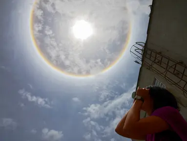 Seorang wanita mengamati fenomena Halo Matahari yang terjadi di atas langit kota Caracas, ibu kota Venezuela, 10 Mei 2016. Fenomena langka itu dinamakan Halo Matahari yang terbentuk akibat refleksi dari kristal es. (Juan BARRETO/AFP)