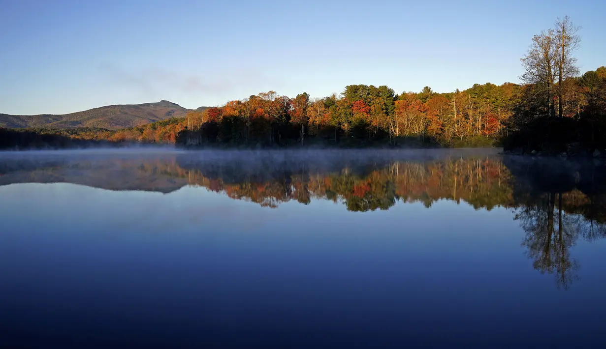 Price Lake memantulkan dedaunan musim gugur saat matahari terbit di sepanjang Blue Ridge Parkway dekat Blowing Rock, North California, saat musim gugur tiba, pada 19 Oktober 2021. (AP Photo/Gerry Broome)