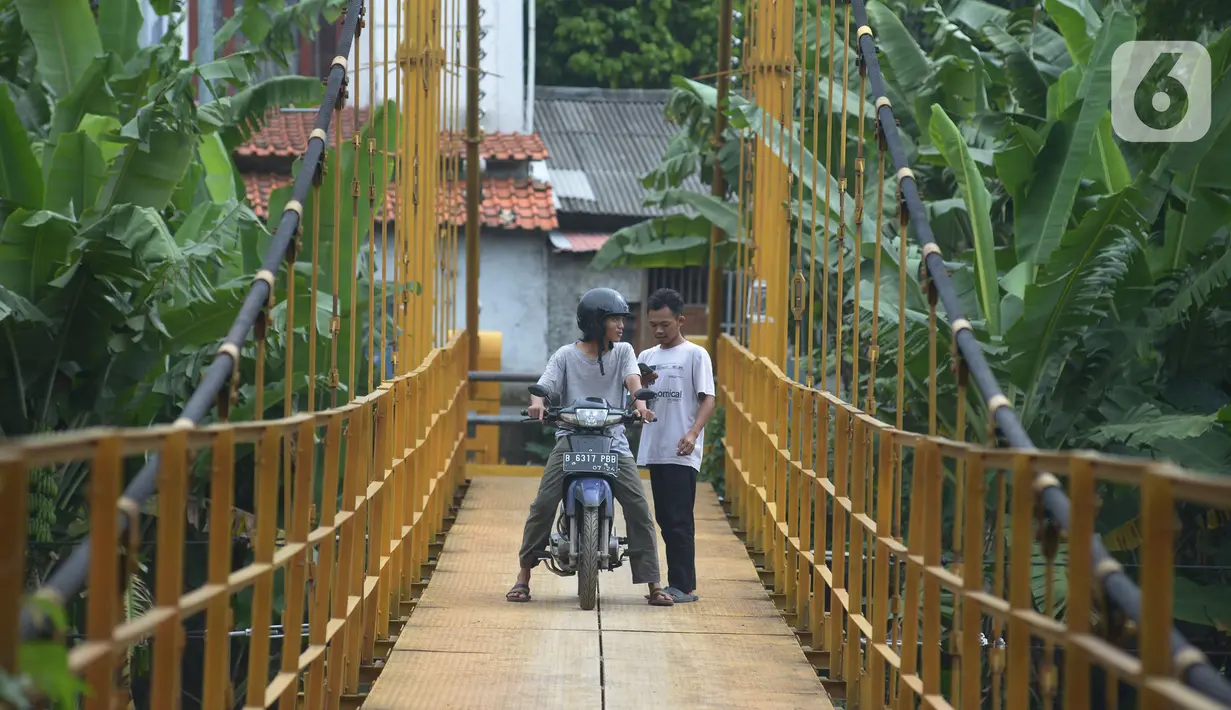 Pengendara motor melintasi jembatan gantung Kuning yang menghubungkan Pasar Minggu Poltangan ke Cililitan Condet, Jakarta, Selasa (28/12/2021). Jembatan gantung Kuning tersebut merupakan jalan umum dan akses jalan warga yang ingin berlalu-lalang. (merdeka.com/Imam Buhori)