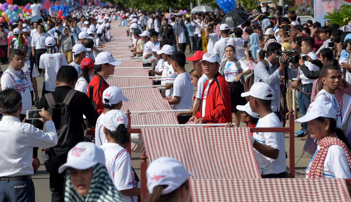 Warga Kamboja membentangkan syal krama sepanjang 1.149,8 meter untuk memecahkan rekor Guinness sebagai syal tenun terpanjang dunia di Phnom Penh, Minggu (1/7). Lebih dari 23.000 orang berpartisipasi membentangkan syal tersebut. (AFP/TANG CHHIN Sothy)