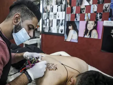 Naim Abdallah saat membuat desain tato wajah macan kumbang dengan kata-kata bahasa Inggris "the hope" di ruang kerjanya di Kota Betlehem di Tepi Barat (24/1/2021). Naim Abdallah merupakan seorang penata rambut dan seniman tato Palestina di Kota Betlehem, Tepi Barat. (AFP/Hazem Bader)