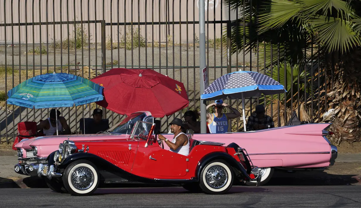 Sebuah kendaraan antik melewati mobil Lowrider yang diparkir di Sunset Boulevard, di lingkungan Echo Park, Los Angeles, pada 18 Juli 2021. Lowrider merupakan gaya dari kendaraan modifikasi yang bermula dari Los Angeles pada pertengahan hingga akhir 1940-an. (AP Photo/Damian Dovarganes)