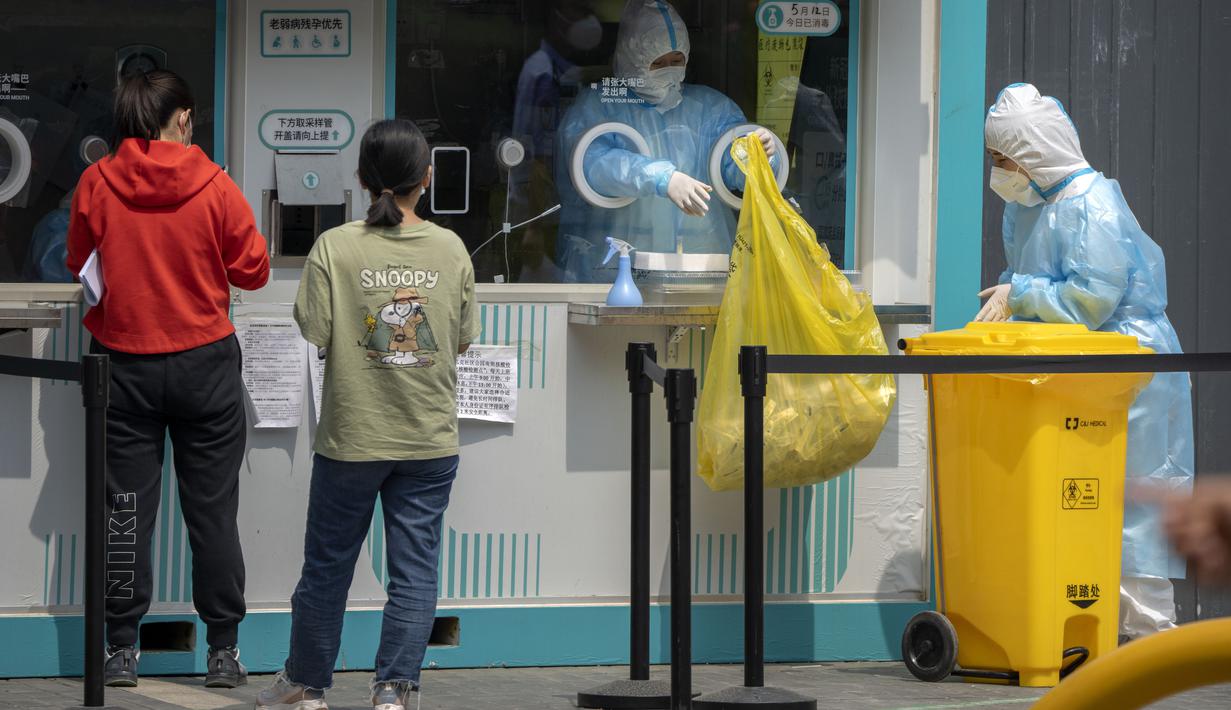 <p>Pekerja yang mengenakan pakaian pelindung menangani kantong sampah di tempat pengujian virus corona di Beijing, Kamis (19/5/2022). Sebagian wilayah Beijing menghentikan pengujian massal harian yang telah dilakukan beberapa minggu terakhir, tetapi banyak tempat pengujian tetap sibuk karena syarat tes negatif COVID-19 dalam 48 jam terakhir untuk memasuki beberapa bangunan di ibu kota China. (AP Photo/Mark Schiefelbein)</p>