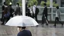 Seorang komuter yang mengenakan masker dan menggunakan payung berjalan jam sibuk di Stasiun Shinagawa, Tokyo, Jumat (1/10/2021). Pemerintah Jepang mencabut keadaan darurat di semua wilayah pada 1 Oktober 2021. (AP Photo/Eugene Hoshiko)