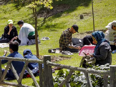 Orang-orang duduk di sebuah taman saat warga Iran berpiknik di luar rumah bersama keluarga dan teman untuk menandai "Sizdeh Bedar" (Hari Alam), 13 hari setelah tahun baru Nowruz Persia, di utara Teheran, Minggu (2/4/2023). (Photo by AFP)