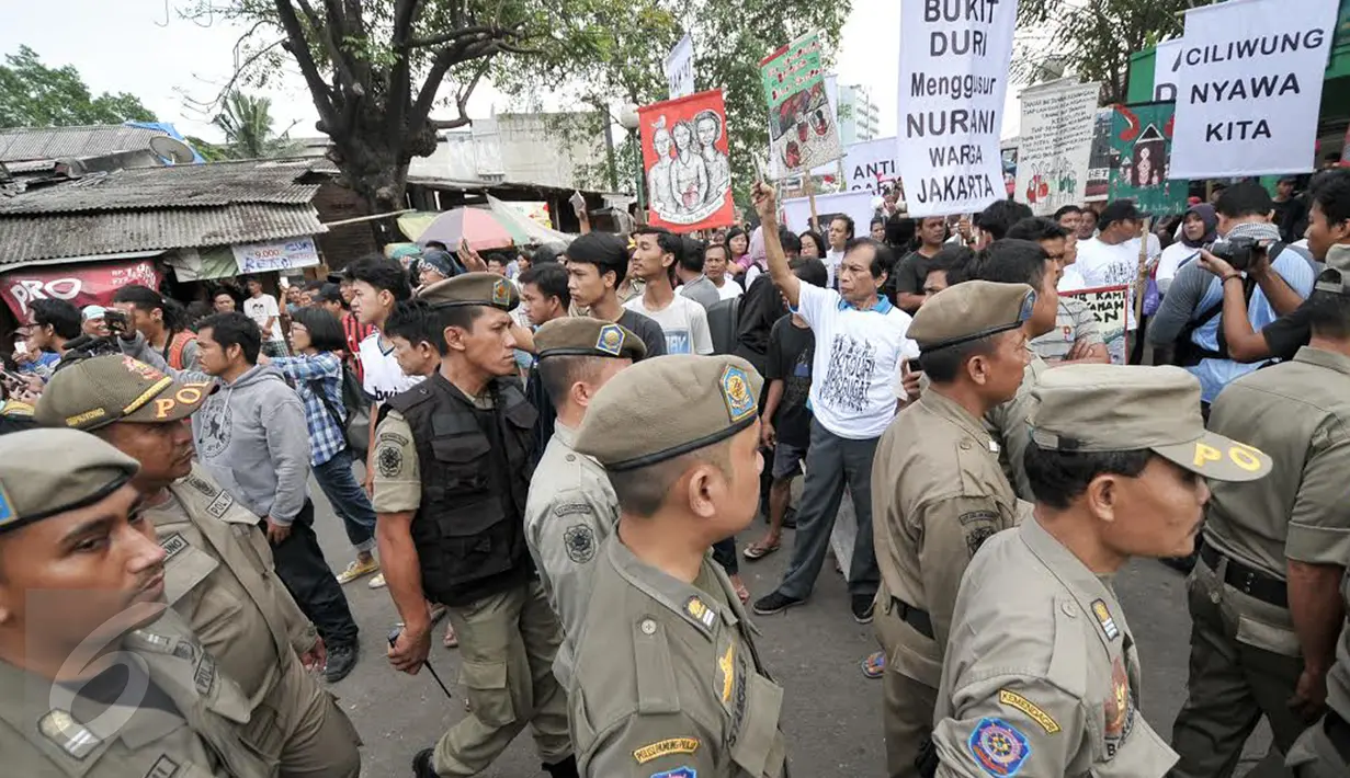 Satpol PP melintas di dekat warga yang menggelar aksi damai di tengah penggusuran kawasan Bukit Duri, Jakarta, Rabu (28/9). Pemprov DKI akhirnya melakukan penertiban pemukiman di Bukit Duri terkait revitalisasi sungai Ciliwung. (Liputan6.com/Yoppy Renato)
