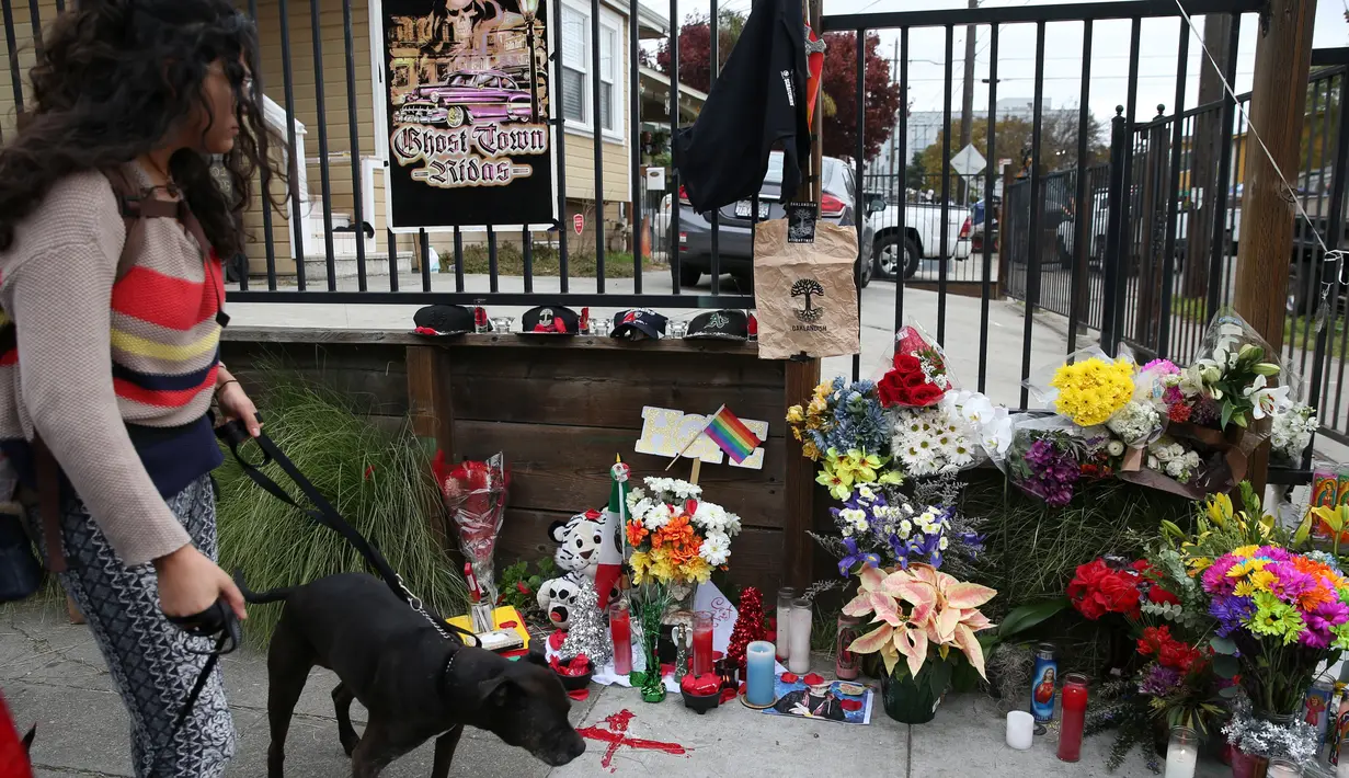 Seorang wanita bersama anjingnya melintas di tempat peringatan Gudang Terbakar di California, AS, Senin (5/12). Warga bersimpati atas peristiwa kebakaran gudang dengan memberikan bunga dan benda-benda lainnya. (REUTERS / Lucy Nicholson)
