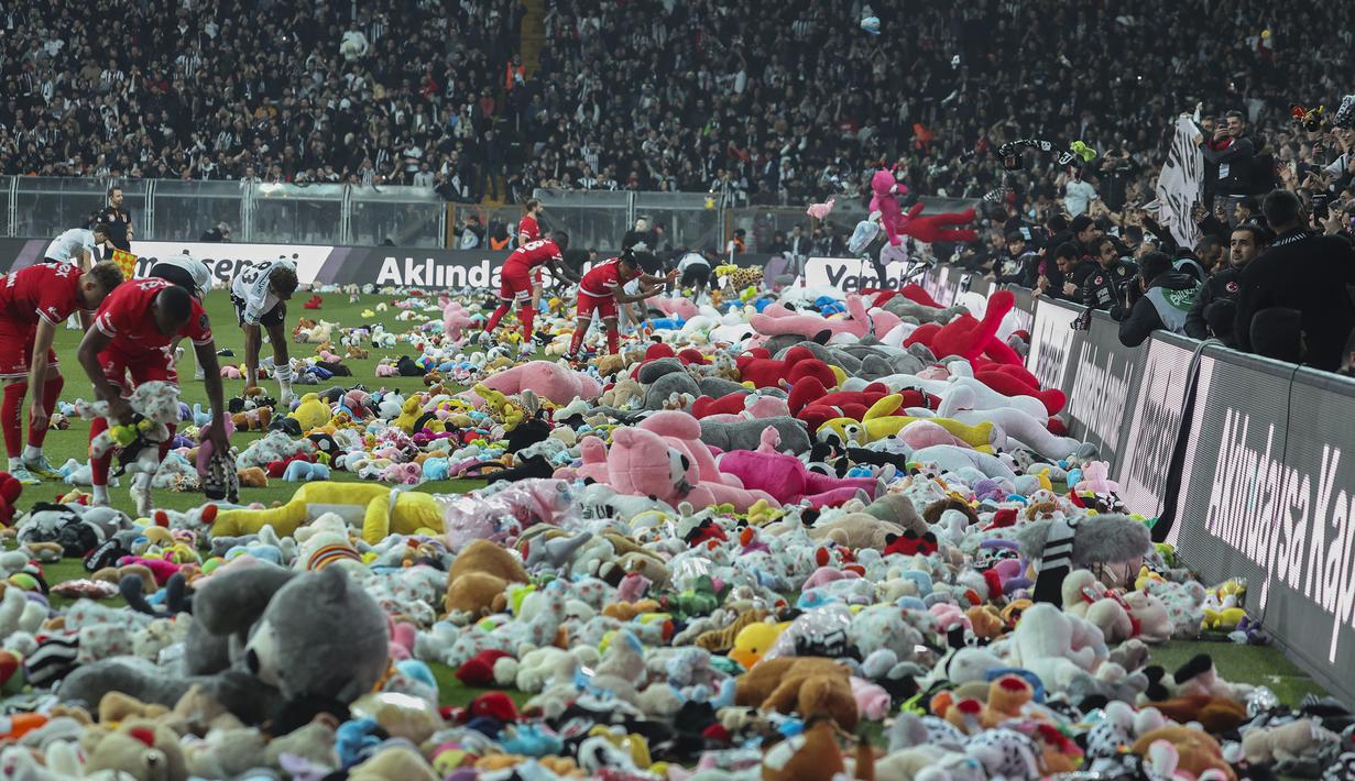 Pemain Besiktas dan Antalyaspor dibantu petugas mengumpulkan boneka yang dilemparkan oleh penonton pada laga lanjutan Liga Turki 2022/2023 yang berlangsung di Stadion Vodafone, Istanbul, Minggu (27/02/2023). Aksi tersebut ditujukan sebagai bentuk sumbangan untuk anak-anak korban gempa Turki. (AP Photo)