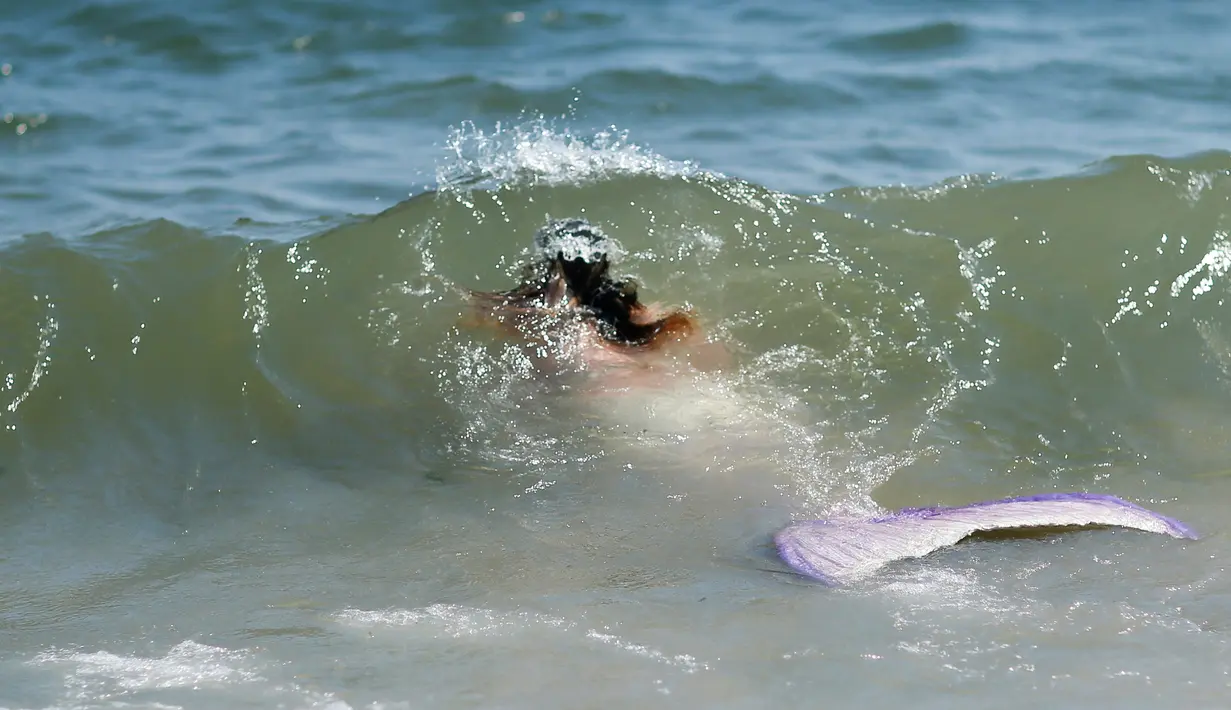 Seorang peserta berpakaian seperti putri duyung berenang di pantai saat mengikuti parade Mermaid, Brooklyn , New York , (18/6).Parade ini diikuti lebih dari 3000 orang peserta yang mengenakan busana bertema Mermaid. (REUTERS / Eduardo Munoz)