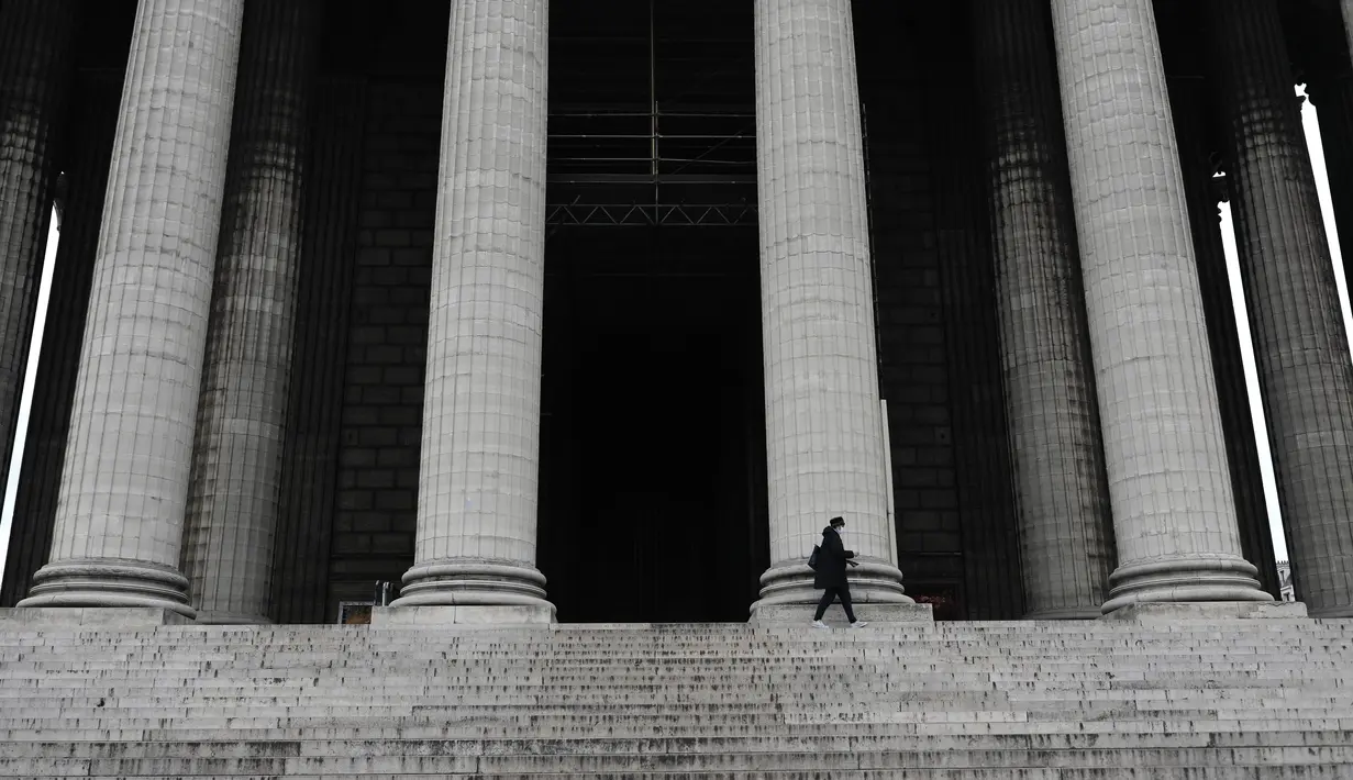 Seorang wanita berjalan di depan gereja La Madeleine di Paris (22/3/2021).  Penduduk Paris dan beberapa wilayah Prancis lainnya menghabiskan akhir pekan pertama mereka di bawah penguncian terbatas selama sebulan.  (AP Photo/Lewis Joly)
