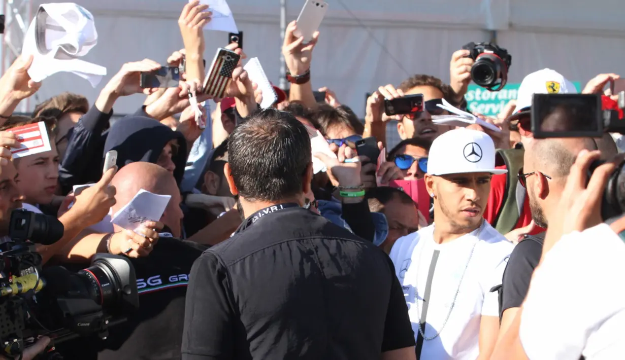 Lewis Hamilton dengan kawalan ketat pihak keamanan F1 melayani permintaan tanda tangan dari ratusan fans yang menanti di gerbang masuk arena Sirkuit Monza. (Bola.com/Reza Khomaini)