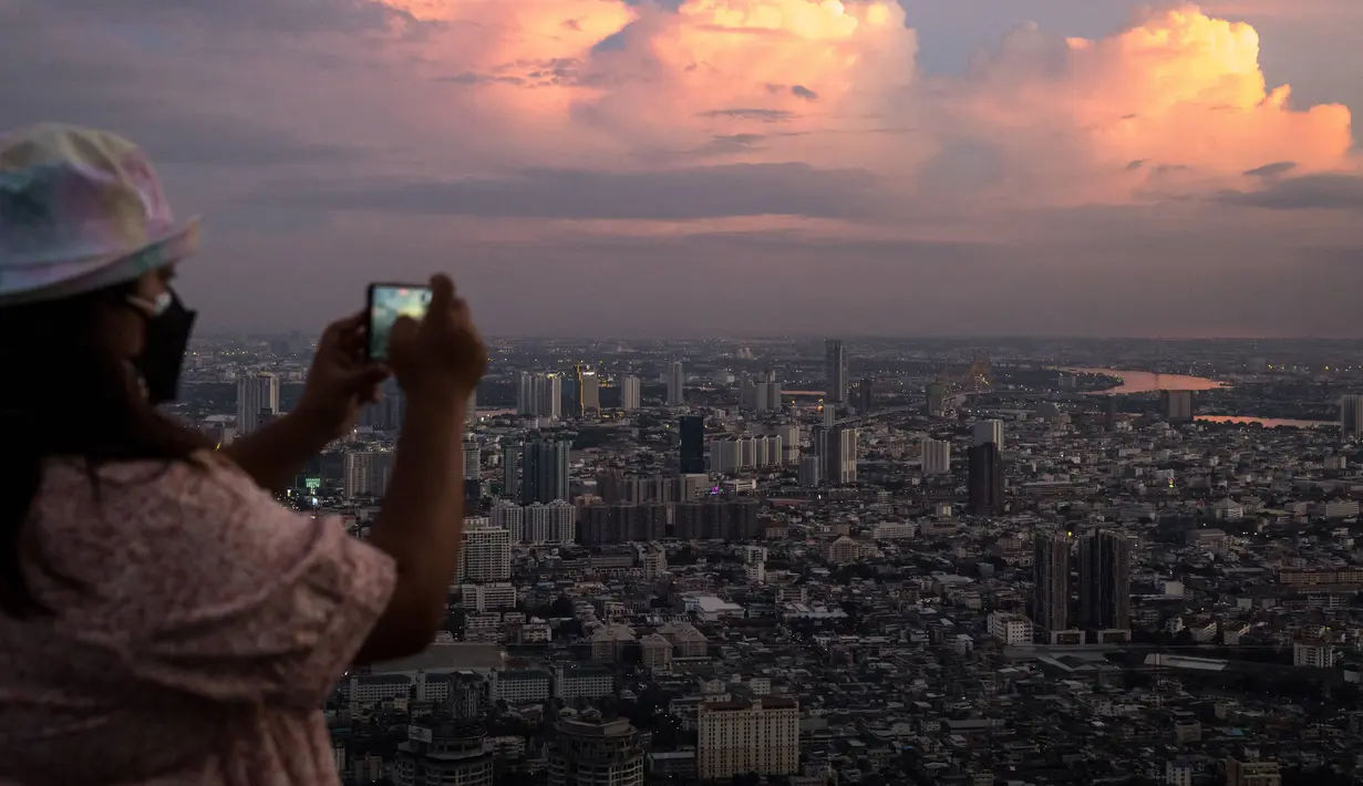 Seorang wanita mengambil foto cakrawala dari dek observasi pencakar langit King Power Mahanakhon saat matahari terbenam di Bangkok, Thailand pada 25 Oktober 2021. Gedung yang dibuka pada tahun 2017 lalu ini memiliki 77 lantai dengan tinggi 324 meter. (Jack TAYLOR / AFP)