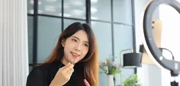 Ilustrasi seorang perempuan sedang memakai lip tint di depan kamera dan ring light.