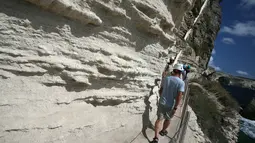Turis menyusuri jalan setapak di kaki tebing sebelum menaiki tangga Raja Aragon di Bonifacio di pulau Corsica, Mediterania Prancis (19/9/2021). Tangga Raja Aragon digali dengan tangan di tebing batu kapur di suatu malam oleh pasukan Raja Aragon tahun 1420. (AFP/Pascal Pochard-Casabianca)