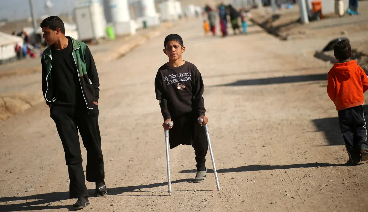 Jasim Abudllah berjalan menggunakan tongkat bersama temannya di kamp Debaga, di pinggiran Erbil, Irak (24/11). Walau hanya memiliki satu kaki, Jasim tetap semangat untuk bermain seperti teman-temannya. (Reuters/Mohammed Salem)