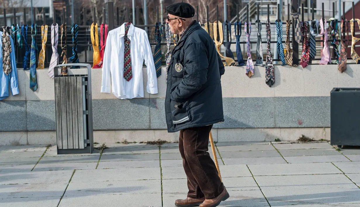 Pejalan kaki melewati dasi yang digantung di pagar luar markas pemerintah Kosovo, Selasa (26/12). Pendemo merasa PM Ramush Haradinaj yang meminta kenaikan gaji karena butuh berpakaian bagus sebagai bagian dari pekerjaan, tak masuk akal. (AP/Visar Kryeziu)