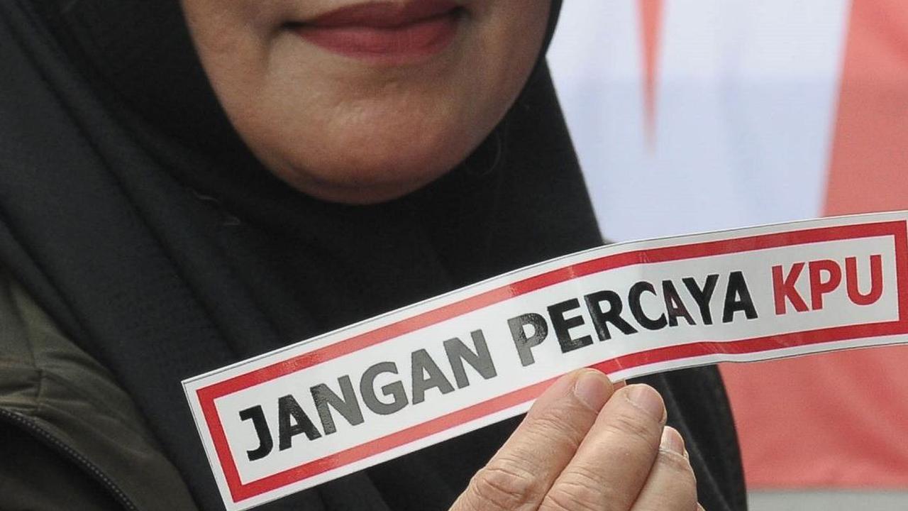 Pendemo menunjukkan sebuah label bertuliskan "Jangan Percaya KPU" saat melakukan aksi di depan Kantor Komisi Pemilihan Umum (KPU), Jakarta, Senin (18/3/2024). Foto: merdeka.com / Imam Buhori
