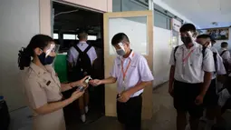 Guru dengan mengenakan pelindung wajah memberikan cairan pembersih tangan kepada siswa sebelum kelas di Samkhok School di Pathum Thani, Bangkok, Rabu (1/7/2020). Thailand telah memulai fase kelima relaksasi pembatasan covid-19 yang memungkinkan kembali dibukanya sekolah-sekolah. (AP/Sakchai Lalit)