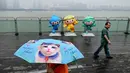 Seorang wanita yang membawa payung berjalan melewati maskot Asian Games 2022, Chenchen, Congcong, dan Lianlian, di sepanjang jalur pejalan kaki sungai Qiantang di Hangzhou, provinsi Zhejiang, China, pada 22 September 2023. (MANAN VATSYAYANA/AFP)