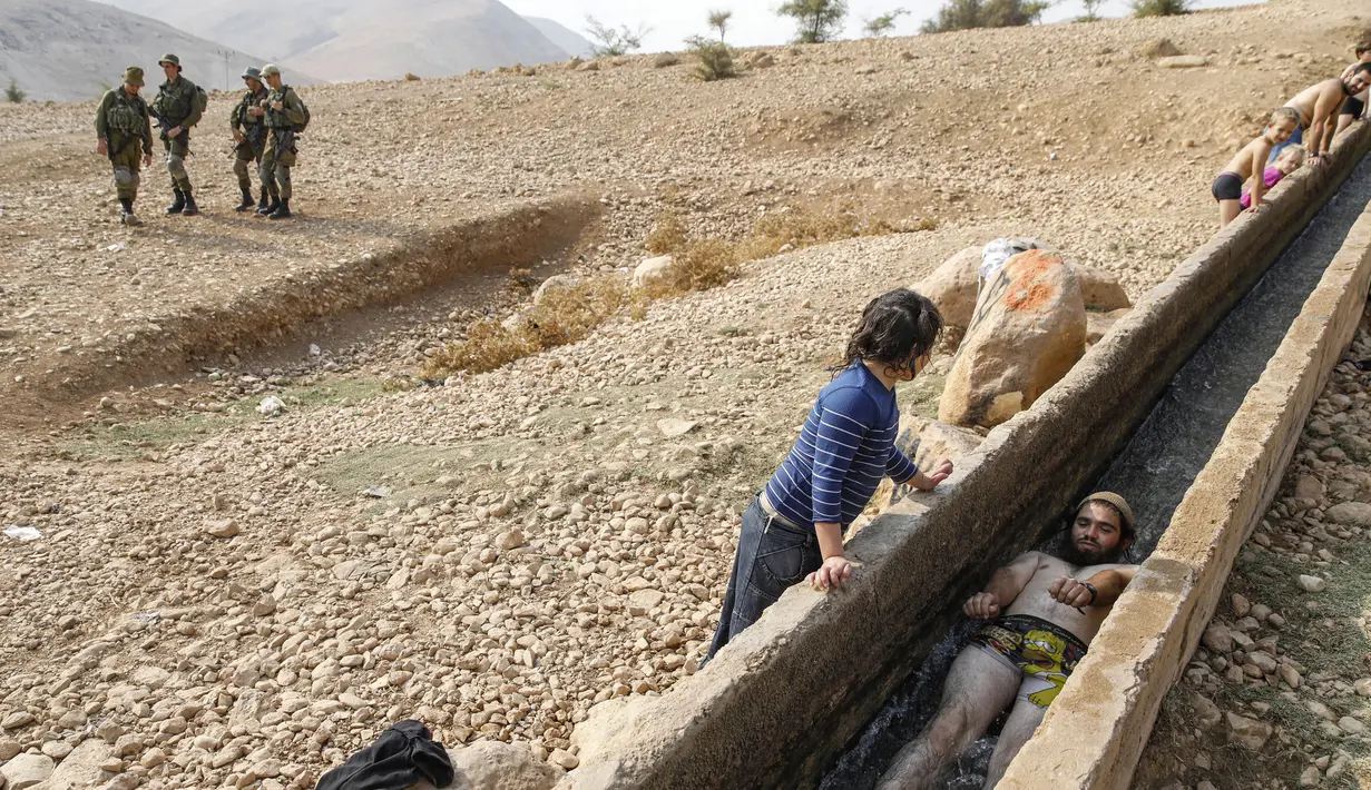 Tentara Israel berjaga-jaga saat warganya asyik bermain air di sebuah kanal kecil di Desa Al-Auja selama perayaan keagamaan Yahudi dalam Festival Sukkot di Tepi Barat (17/10/2019). (AFP Photo/Menahem Kahana)