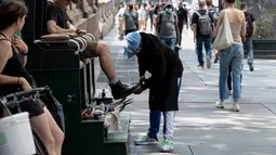 Seorang pria menyemir sepatunya pada hari yang hangat di New York City (7/6/2021). Cuaca yang hangat di New York dimanfaatkan warga untuk membaca buku hingga berjalan-jalan. (AFP/Angela Weiss)