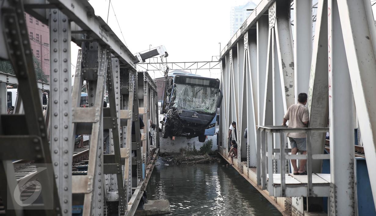 Petugas mengevakuasi bus transjakarta yang terperosok ke sungai usai ditabrak kereta Senja Utama Solo di perlintasan Jalan Mangga Dua, Jakarta, Kamis (19/5). Tak ada korban jiwa, namun sopir Transjakarta mengalami luka berat. (Liputan6.com/Faizal Fanani)