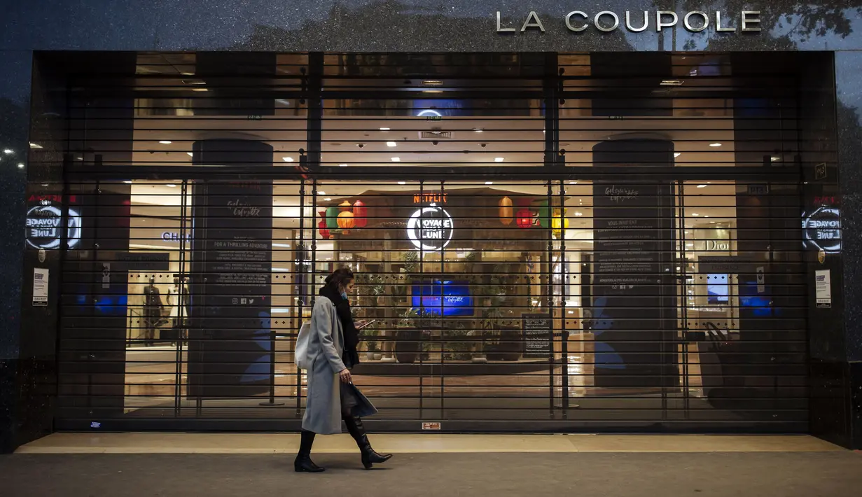 Seorang wanita berjalan di dekat pintu masuk Galeries Lafayette yang tertutup di pusat kota Paris, Jumat (30/10/2020). Penguncian juga melarang orang masuk melampaui satu kilometer dari rumah mereka kecuali untuk pergi ke sekolah atau beberapa alasan penting lainnya. (AP Photo/Lewis Joly)