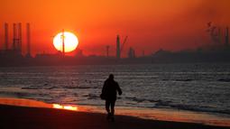 Seorang pria berjalan di dekat Industri pelabuhan Dunkirk saat matahari terbenam di Leffrinckoucke, Prancis (25/2). (Reuters/Pascal Rossignol)