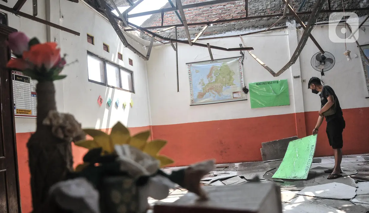 Penjaga sekolah berada di salah satu ruang kelas yang rusak akibat terjangan angin kencang di Sekolah Dasar Negeri (SDN) Pancoranmas 3, Depok, Jawa Barat, Minggu (24/7/2022). Puing-puing sisa bangunan yang ambruk pun masih berserakan di ruang kelas. (merdeka.com/Iqbal S. Nugroho)
