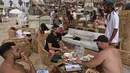 Orang-orang bersantai di bar pantai di kota pesisir Israel Tel Aviv (19/4/2021). Pemerintah Israel mencabut kewajiban memakai masker setelah 81 persen penduduk dewasa menerima vaksin Covid-19. (AFP/menahem kahana)