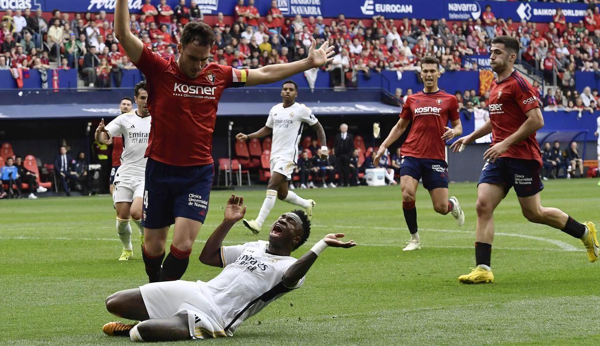 Pemain Real Madrid, Vinicius Junior, terjatuh saat berebut bola dengan pemain Osasuna, Alejandro Catena, pada laga pekan ke-29 La Liga 2023/2024 di Stadion El Sadar, Sabtu (16/03/2024). (AP Photo/Alvaro Barrientos)