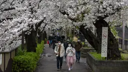 Orang-orang yang memakai masker pelindung untuk membantu mengekang penyebaran virus corona berjalan di bawah  bunga sakura Minggu 28 Maret 2021 di Tokyo, Minggu (28/3/2021). (AP Photo/Kiichiro Sato)