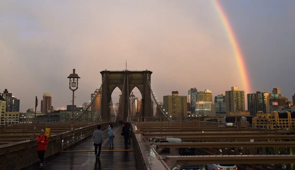 Warga beraktivitas saat pelangi terlihat dari Jembatan Brooklyn di New York City, AS (15/5). Jembatan ini selesai dibangun 1883 dan menghubungkan borough Manhattan dan Brooklyn di New York City melintasi Sungai East. (AFP Photo/Hector Retamal)