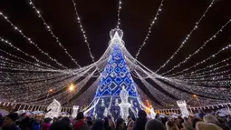 Orang-orang berjalan di dekat pohon Natal raksasa yang menerangi Alun-Alun Katedral di Vilnius, Lithuania, Minggu (1/12/2019). Secara tradisi, pohon Natal Vilnius biasanya berupa rangka logam yang ditutupi dengan dekorasi dan cabang-cabang pohon dari hutan. (AP/Mindaugas Kulbis)