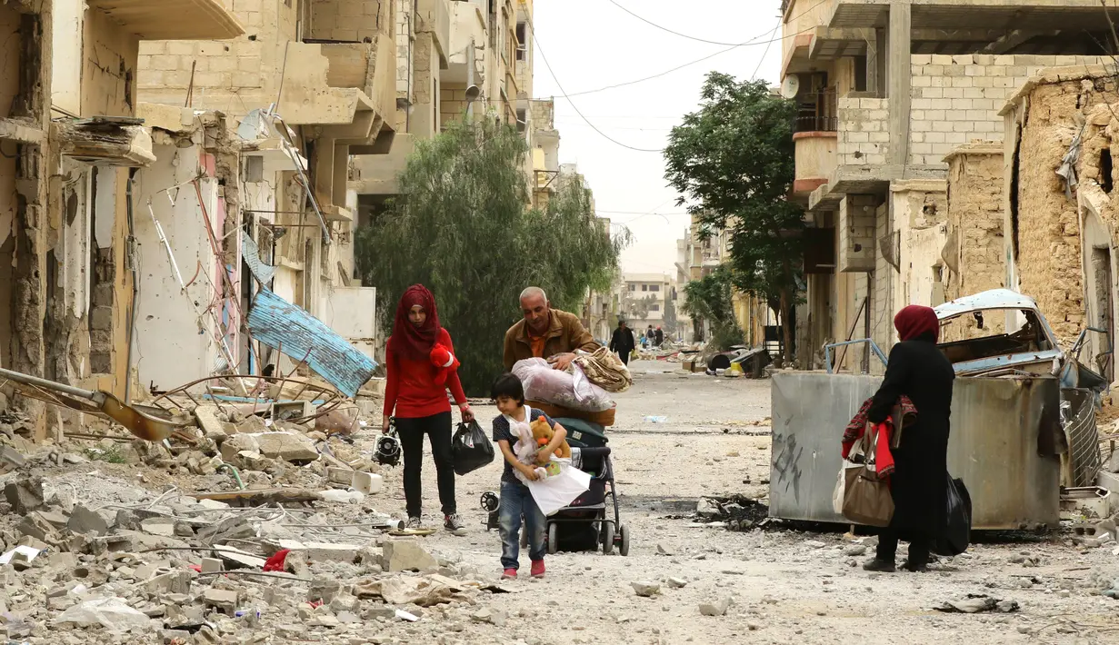 Sebuah keluarga melewati reruntuhan bangunan untuk kembali ke rumah mereka di kota modern Palmyra, berdekatan dengan kota kuno Suriah, Sabtu (9/4). Warga kembali ke rumah mereka setelah dibebaskannya dua kota tersebut dari tangan ISIS. (Louai BESHARA/AFP)