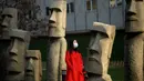 Seorang perempuan yang mengenakan masker berjalan melewati replika patung raksasa 'Moai' Pulau Paskah di Beijing pada Rabu (4/11/2020). Pulau Paskah yang berada di Negara Chile terkenal oleh patung kepala yang dipahat dari batu. (Photo by Noel Celis / AFP)