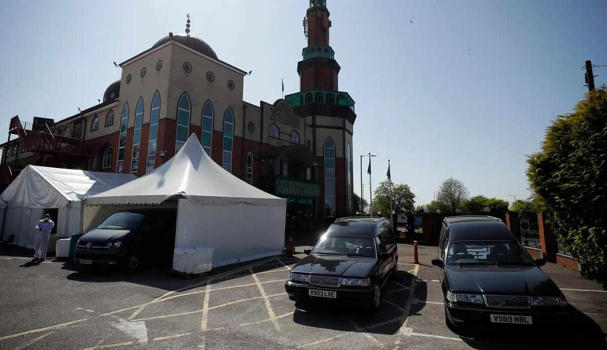 Sukarelawan berpakaian pelindung berjalan di halaman parkir Central Jamis Mosque Ghamkol Sharif di Birmingham, Inggris pada 24 April 2020. Saat masjid itu tutup selama Ramadan di tengah pandemi, tempat parkirnya digunakan menjadi kamar mayat sementara untuk korban corona Covid-19. (AP/Matt Dunham)