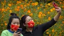 Seorang wanita mengenakan masker bertuliskan "I love you China" berpose untuk selfie dengan bunga mekar di taman umum di Beijing, Sabtu (2/10/2021). Pengunjung memadati taman dan lokasi wisata di Beijing saat China merayakan hari kedua masa libur Hari Nasional. (AP Photo/Mark Schiefelbein)