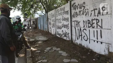 Pengguna jalan melihat mural di kawasan Citayam, Depok, Jawa Barat, Rabu (25/8/2021). Mural tersebut merupakan wujud ekspresi dari sejumlah seniman serta sebagai media penyampaian kritik sosial kepada pemerintah di tengah pandemi COVID-19. (Liputan6.com/Herman Zakharia)